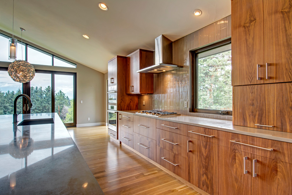 Inspiration for a large contemporary galley kitchen pantry in Denver with an undermount sink, flat-panel cabinets, medium wood cabinets, granite benchtops, beige splashback, ceramic splashback, stainless steel appliances, light hardwood floors, with island and brown floor.