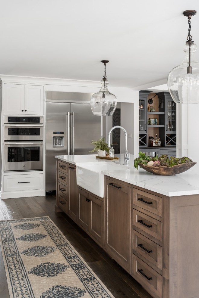 Design ideas for a large country l-shaped open plan kitchen in Chicago with a farmhouse sink, shaker cabinets, white cabinets, quartz benchtops, white splashback, window splashback, stainless steel appliances, medium hardwood floors, with island, brown floor and white benchtop.