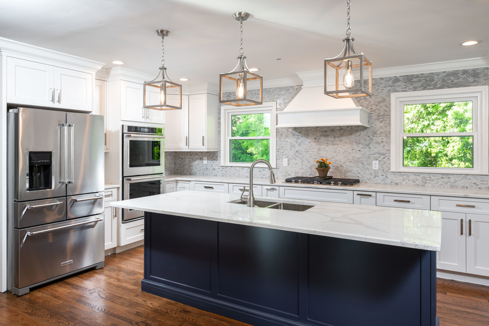 Kitchen - large transitional l-shaped medium tone wood floor and brown floor kitchen idea with a double-bowl sink, shaker cabinets, white cabinets, quartz countertops, gray backsplash, mosaic tile backsplash, stainless steel appliances, an island and white countertops