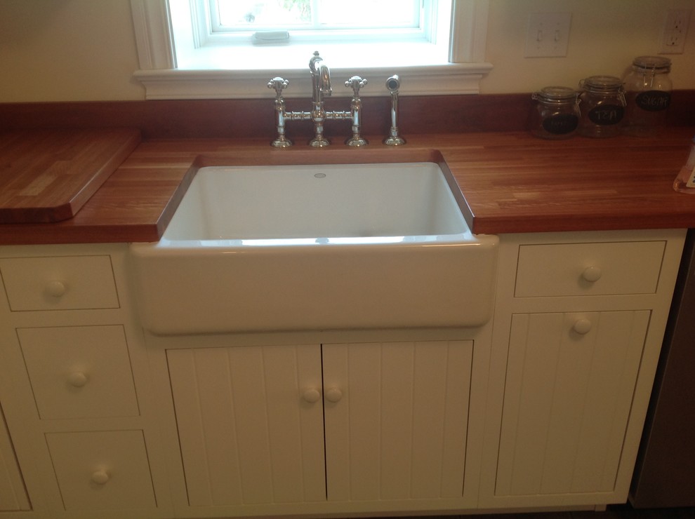 Enclosed kitchen - mid-sized l-shaped medium tone wood floor enclosed kitchen idea with a farmhouse sink, flat-panel cabinets, white cabinets, wood countertops, beige backsplash, stainless steel appliances and no island