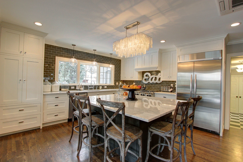 Large transitional l-shaped dark wood floor enclosed kitchen photo in Denver with an undermount sink, shaker cabinets, white cabinets, marble countertops, brown backsplash, subway tile backsplash, stainless steel appliances and an island