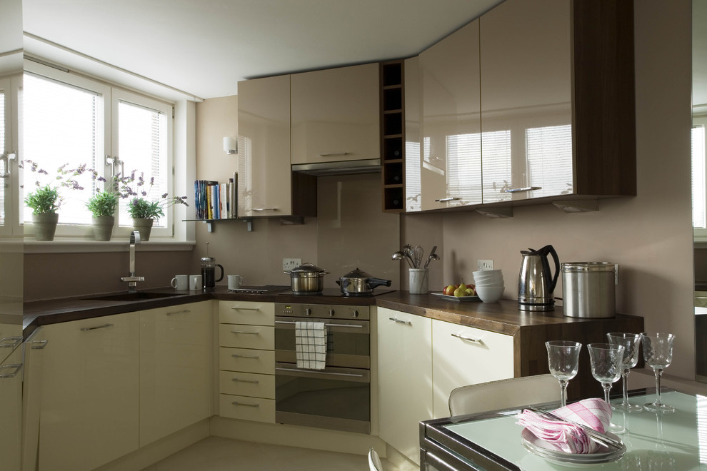 This is an example of an eclectic eat-in kitchen in London with flat-panel cabinets, beige cabinets, brown splashback and stainless steel appliances.