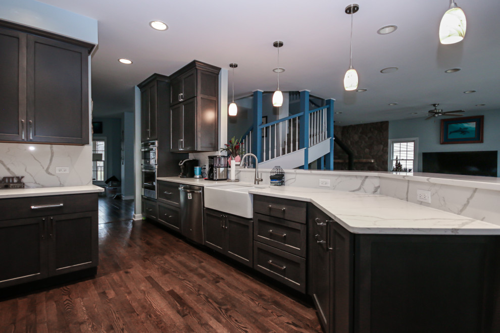Large transitional u-shaped medium tone wood floor eat-in kitchen photo in Chicago with a farmhouse sink, shaker cabinets, dark wood cabinets, quartz countertops, white backsplash, quartz backsplash, stainless steel appliances, a peninsula and white countertops
