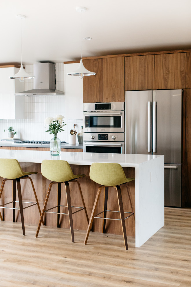 Photo of a medium sized midcentury l-shaped open plan kitchen in Seattle with flat-panel cabinets, medium wood cabinets, engineered stone countertops, white splashback, stainless steel appliances, an island and white worktops.