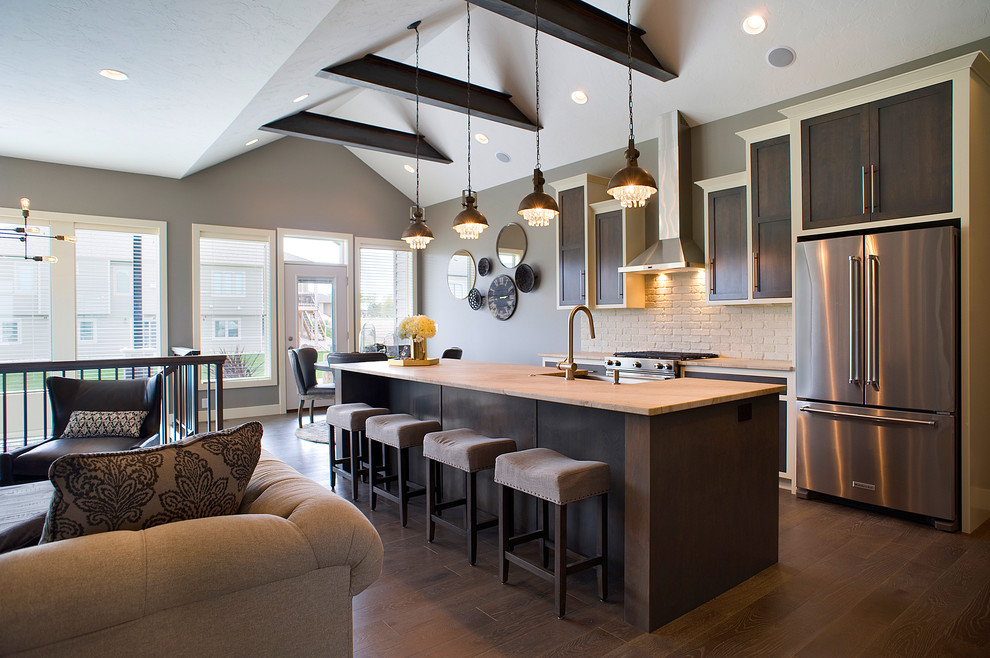 Example of a mid-sized transitional l-shaped dark wood floor and brown floor eat-in kitchen design with a farmhouse sink, recessed-panel cabinets, dark wood cabinets, granite countertops, beige backsplash, brick backsplash, stainless steel appliances and an island