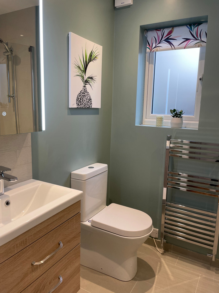 Small contemporary family bathroom in London with flat-panel cabinets, light wood cabinets, a built-in bath, a shower/bath combination, a one-piece toilet, beige tiles, porcelain tiles, blue walls, porcelain flooring, a wall-mounted sink, beige floors, a hinged door, a single sink and a floating vanity unit.