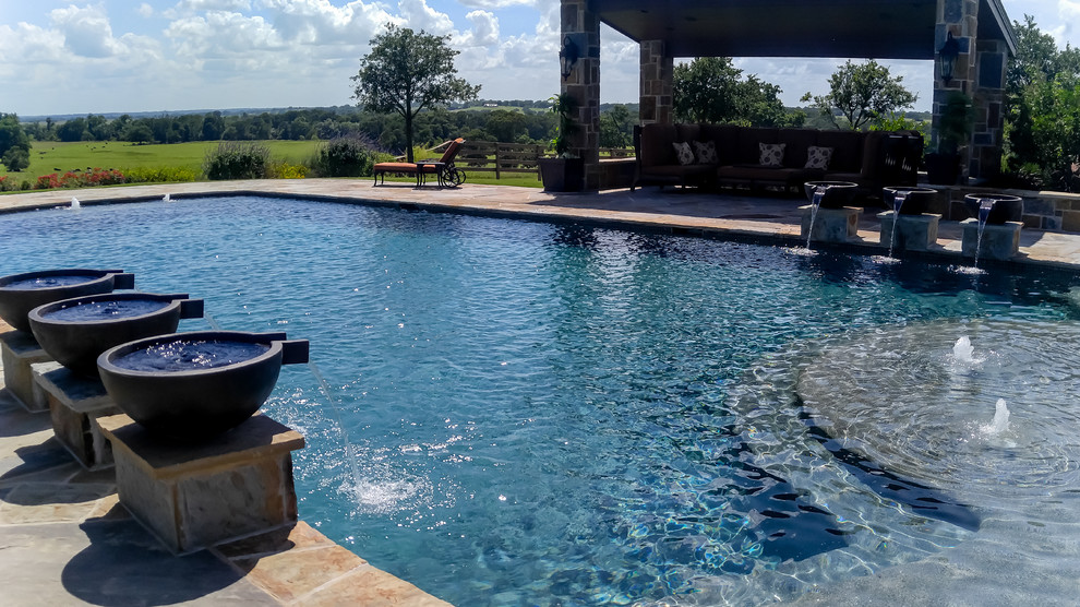 Large traditional backyard rectangular lap pool in Dallas with a water feature and natural stone pavers.
