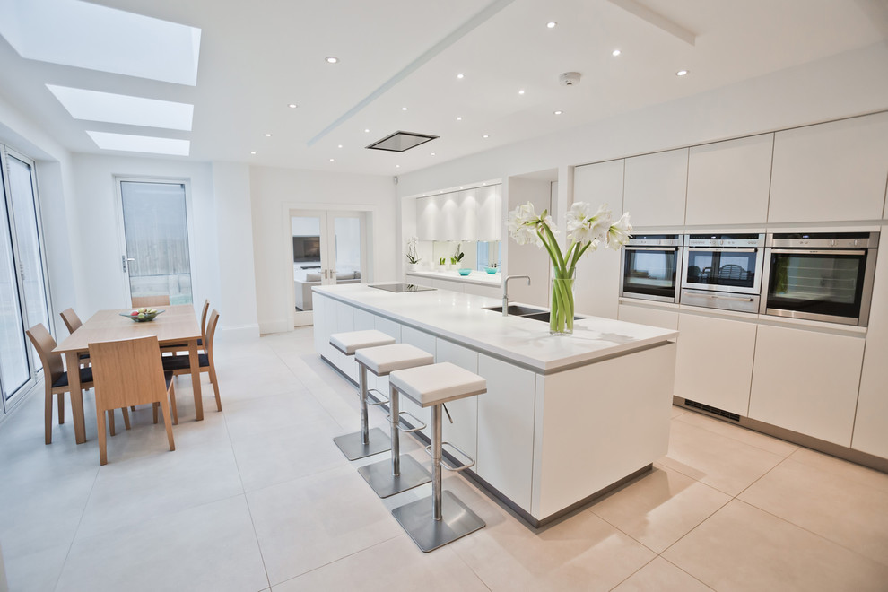 Inspiration for a modern galley eat-in kitchen in Manchester with a double-bowl sink, flat-panel cabinets, white cabinets, mirror splashback, with island, beige floor and white benchtop.