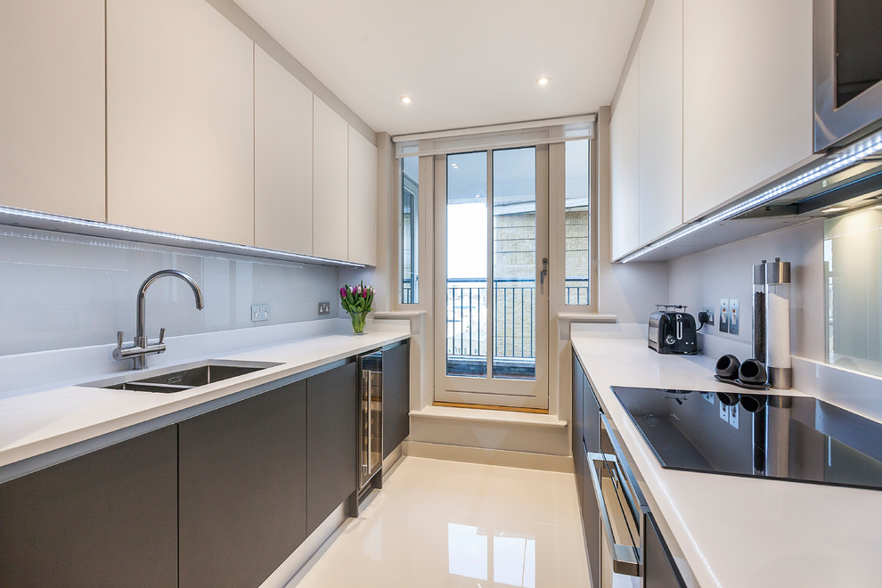 Small contemporary galley separate kitchen in London with a drop-in sink, flat-panel cabinets, white cabinets, quartzite benchtops, white splashback, glass sheet splashback, panelled appliances, porcelain floors and no island.