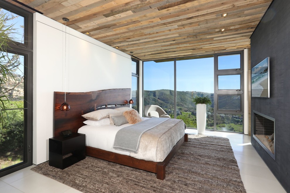 Inspiration for a large contemporary master bedroom in Orange County with beige walls, porcelain floors, a two-sided fireplace, a plaster fireplace surround and beige floor.