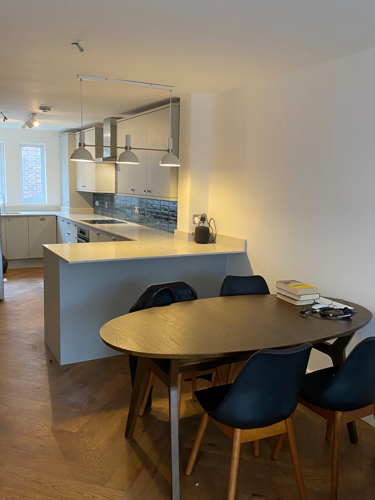 This is an example of a large contemporary u-shaped open plan kitchen in London with a built-in sink, flat-panel cabinets, grey cabinets, quartz worktops, blue splashback, ceramic splashback, black appliances, dark hardwood flooring, a breakfast bar, brown floors and grey worktops.