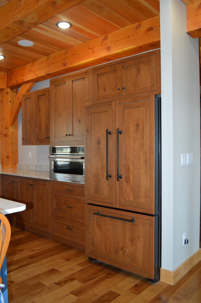 Mid-sized mountain style u-shaped medium tone wood floor, brown floor and exposed beam eat-in kitchen photo with a farmhouse sink, shaker cabinets, medium tone wood cabinets, paneled appliances and an island