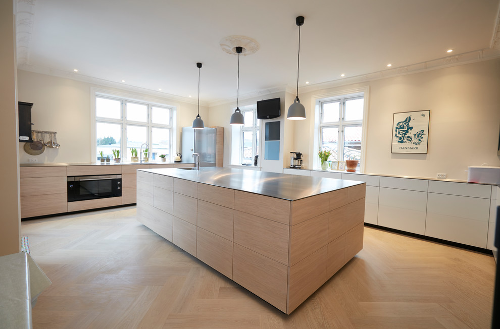 This is an example of a large modern l-shaped kitchen in Copenhagen with flat-panel cabinets, light wood cabinets, stainless steel benchtops, panelled appliances and with island.