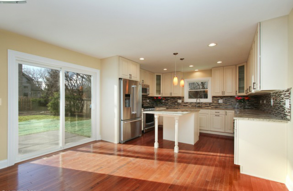 Open concept kitchen - mid-sized transitional u-shaped medium tone wood floor open concept kitchen idea in Chicago with an undermount sink, raised-panel cabinets, white cabinets, granite countertops, multicolored backsplash, matchstick tile backsplash, stainless steel appliances and an island