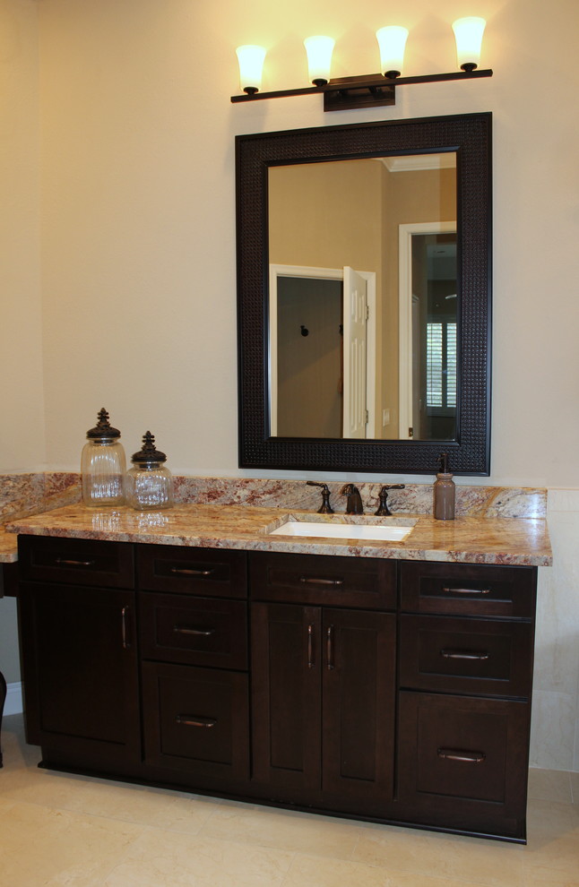 Photo of a transitional master bathroom in Tampa with recessed-panel cabinets, dark wood cabinets, granite benchtops, beige tile, an undermount sink, porcelain tile and porcelain floors.