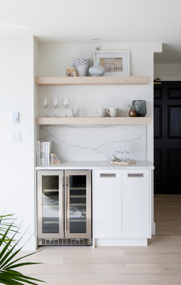 Small scandinavian single-wall home bar in Vancouver with no sink, flat-panel cabinets, white cabinets, white splashback, stone slab splashback, light hardwood floors, beige floor and white benchtop.