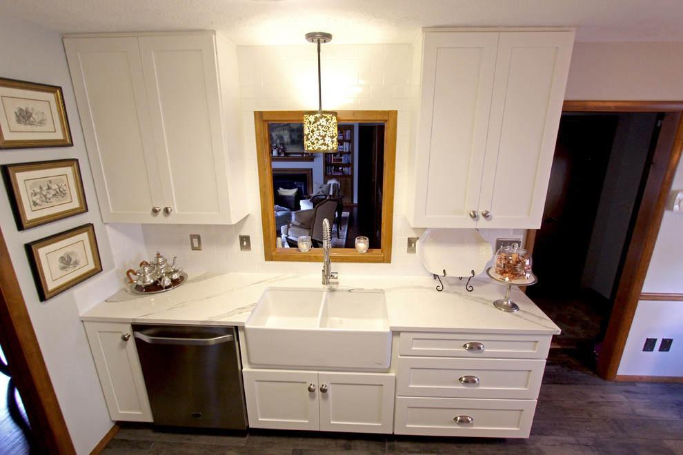 This is an example of a small transitional galley eat-in kitchen in Cleveland with a farmhouse sink, flat-panel cabinets, white cabinets, quartz benchtops, white splashback, subway tile splashback, stainless steel appliances, ceramic floors and no island.