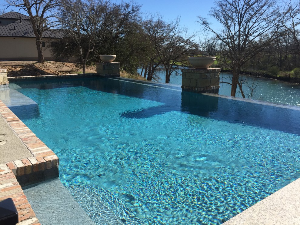 Example of a mid-sized backyard stamped concrete and custom-shaped infinity hot tub design in Austin