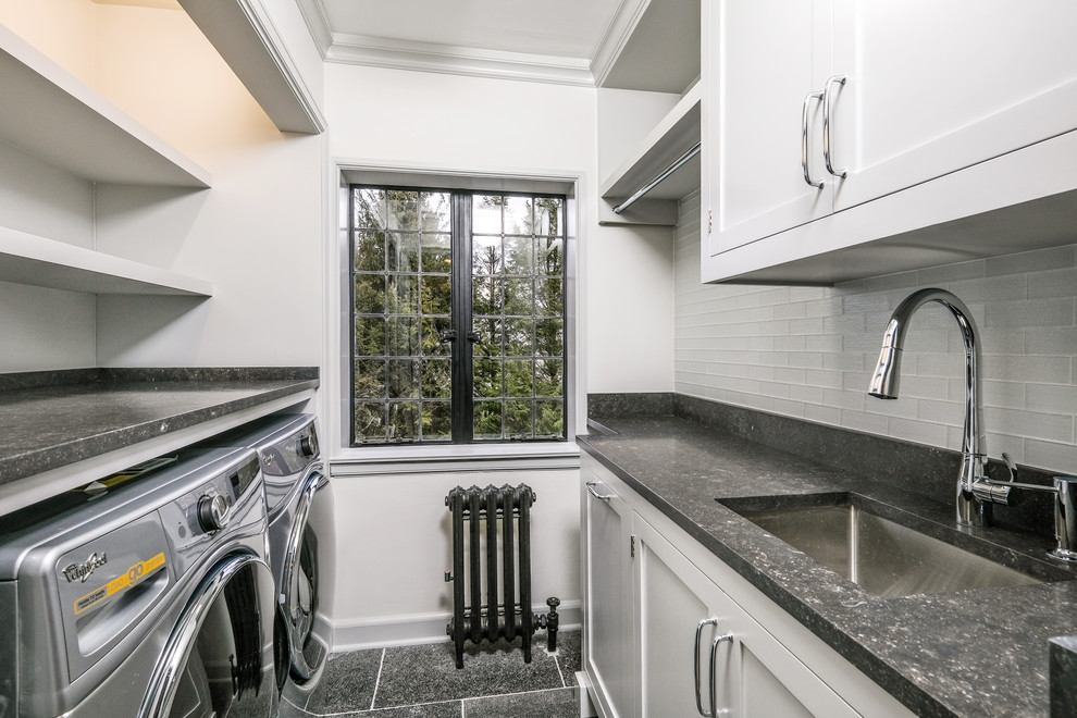 Small traditional single-wall dedicated laundry room in New York with an undermount sink, shaker cabinets, grey cabinets, limestone benchtops, grey walls, limestone floors, a side-by-side washer and dryer, black floor and black benchtop.