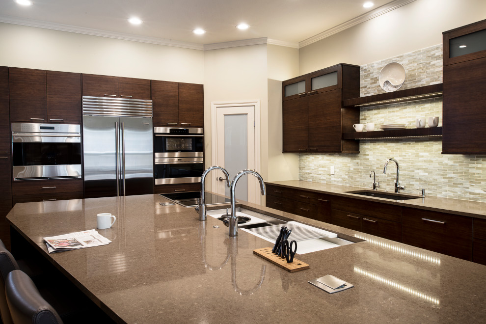 Example of a large transitional medium tone wood floor and brown floor kitchen design with an undermount sink, flat-panel cabinets, brown cabinets, quartzite countertops, beige backsplash, ceramic backsplash, stainless steel appliances, an island and beige countertops