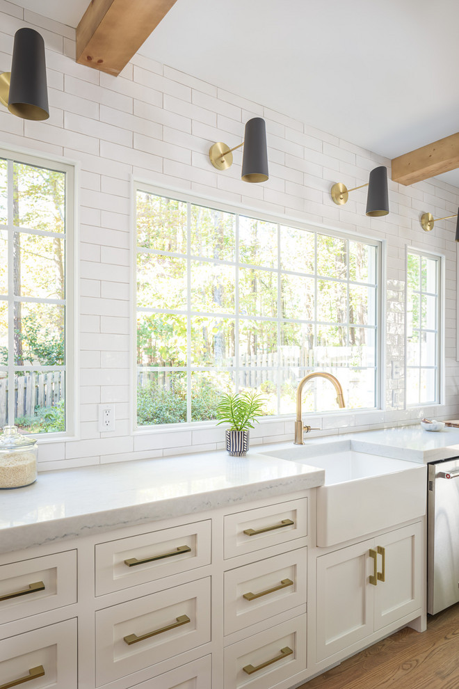 Design ideas for a mid-sized country single-wall open plan kitchen in Raleigh with a farmhouse sink, white cabinets, wood benchtops, white splashback, subway tile splashback, panelled appliances, light hardwood floors, with island, white benchtop and shaker cabinets.