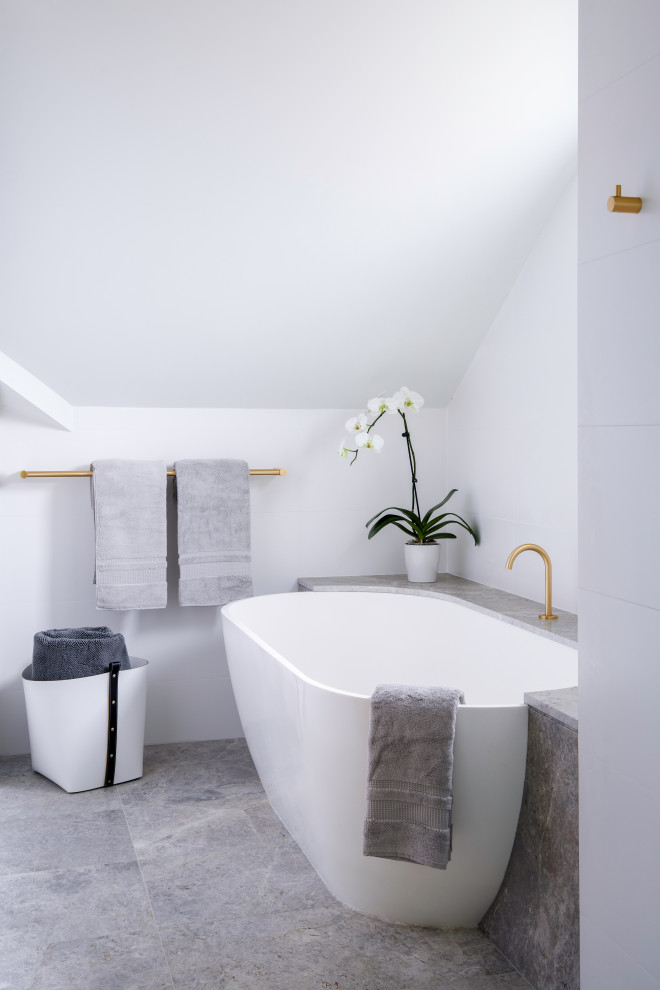 Cette image montre une salle de bain design en bois clair avec un placard à porte plane, une baignoire posée, un carrelage blanc, des carreaux de céramique, un lavabo encastré, un plan de toilette en marbre, un sol gris, un plan de toilette gris, meuble double vasque et meuble-lavabo suspendu.