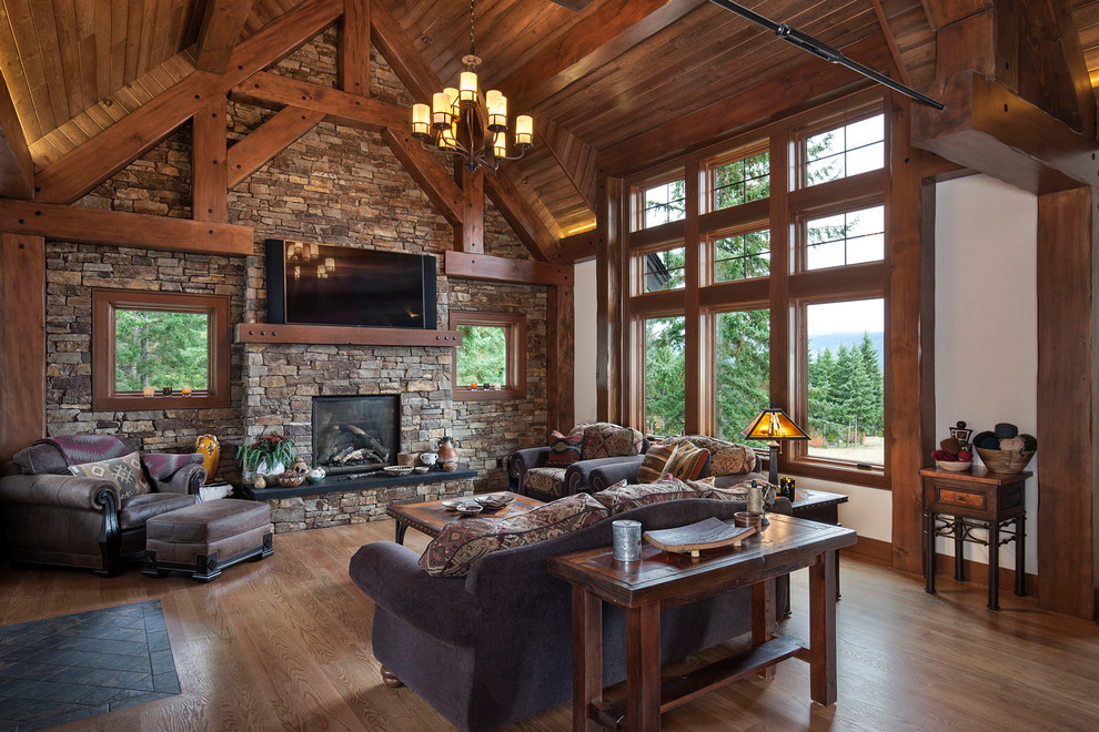 Design ideas for a mid-sized country open concept living room in Seattle with beige walls, medium hardwood floors, a standard fireplace, a stone fireplace surround, a wall-mounted tv and brown floor.