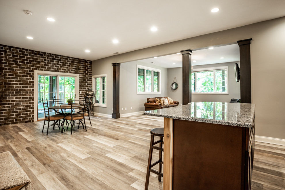 This is an example of a large country walk-out basement in Indianapolis with grey walls, vinyl floors, a standard fireplace, a stone fireplace surround and brown floor.