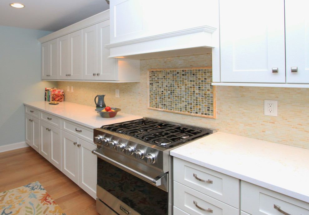 Photo of a mid-sized beach style galley open plan kitchen in Grand Rapids with an undermount sink, shaker cabinets, white cabinets, quartz benchtops, yellow splashback, glass tile splashback, stainless steel appliances, light hardwood floors and with island.
