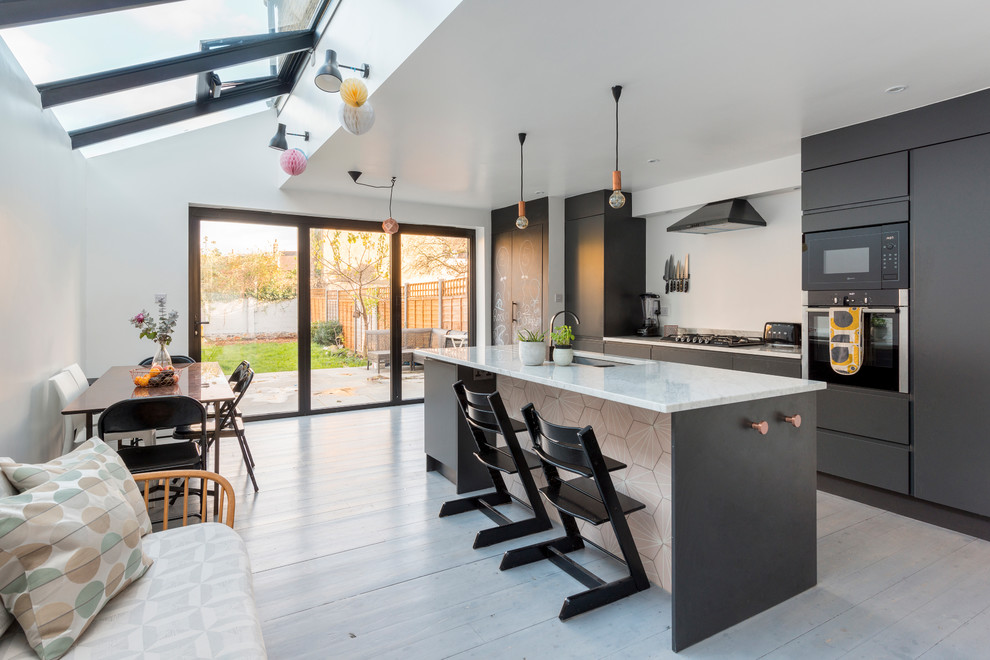 This is an example of a mid-sized contemporary single-wall eat-in kitchen in London with flat-panel cabinets, black cabinets, marble benchtops, light hardwood floors, with island and white floor.