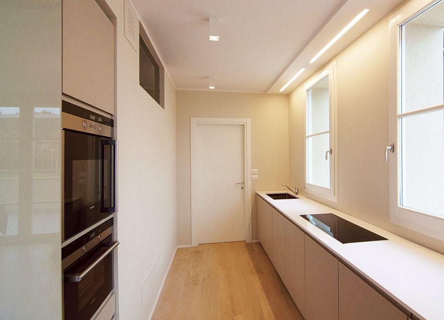 Photo of a small modern galley separate kitchen in Other with a drop-in sink, flat-panel cabinets, white cabinets, quartz benchtops, light hardwood floors and recessed.