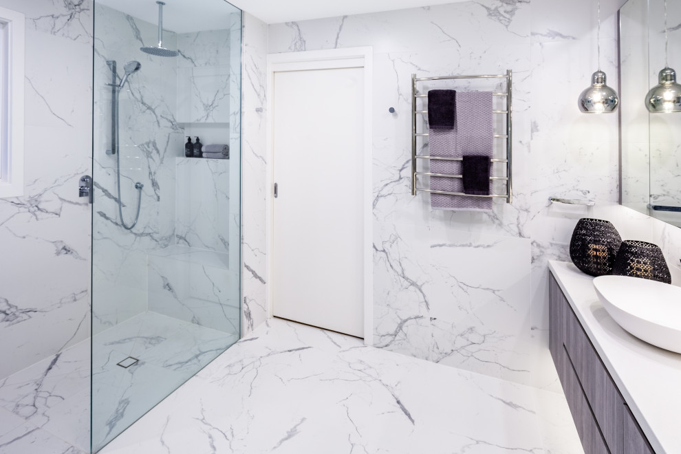 This is an example of a contemporary master bathroom in Melbourne with flat-panel cabinets, medium wood cabinets, a freestanding tub, a curbless shower, a one-piece toilet, white tile, porcelain tile, white walls, porcelain floors, a vessel sink, engineered quartz benchtops, white floor, an open shower, white benchtops, a shower seat, a double vanity and a floating vanity.