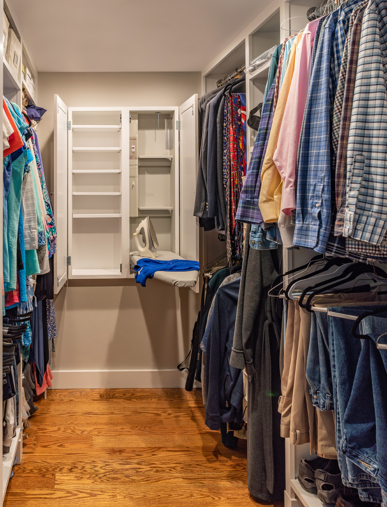 Photo of a mid-sized beach style gender-neutral walk-in wardrobe in Boston with medium hardwood floors, white cabinets and recessed-panel cabinets.