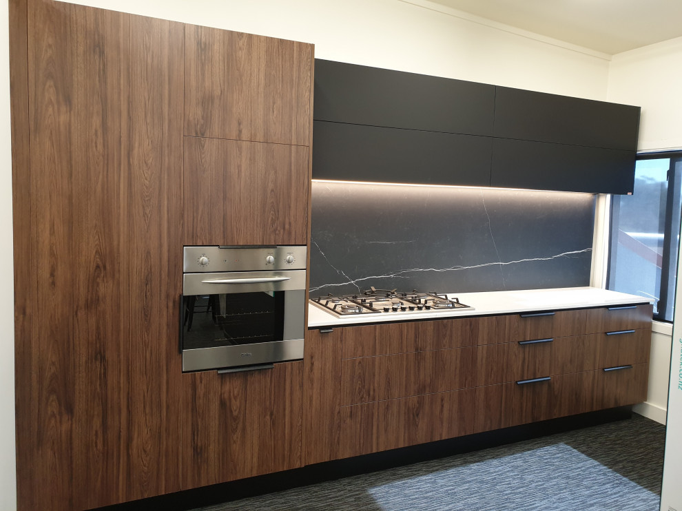 Photo of a mid-sized modern single-wall kitchen pantry in Christchurch with flat-panel cabinets, dark wood cabinets, quartz benchtops, black splashback, porcelain splashback, stainless steel appliances, carpet, no island, black floor and white benchtop.