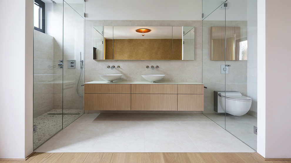 This is an example of a large contemporary bathroom in Berlin with flat-panel cabinets, medium wood cabinets, an alcove shower, a wall-mount toilet, beige tile, ceramic tile, white walls, ceramic floors and a vessel sink.