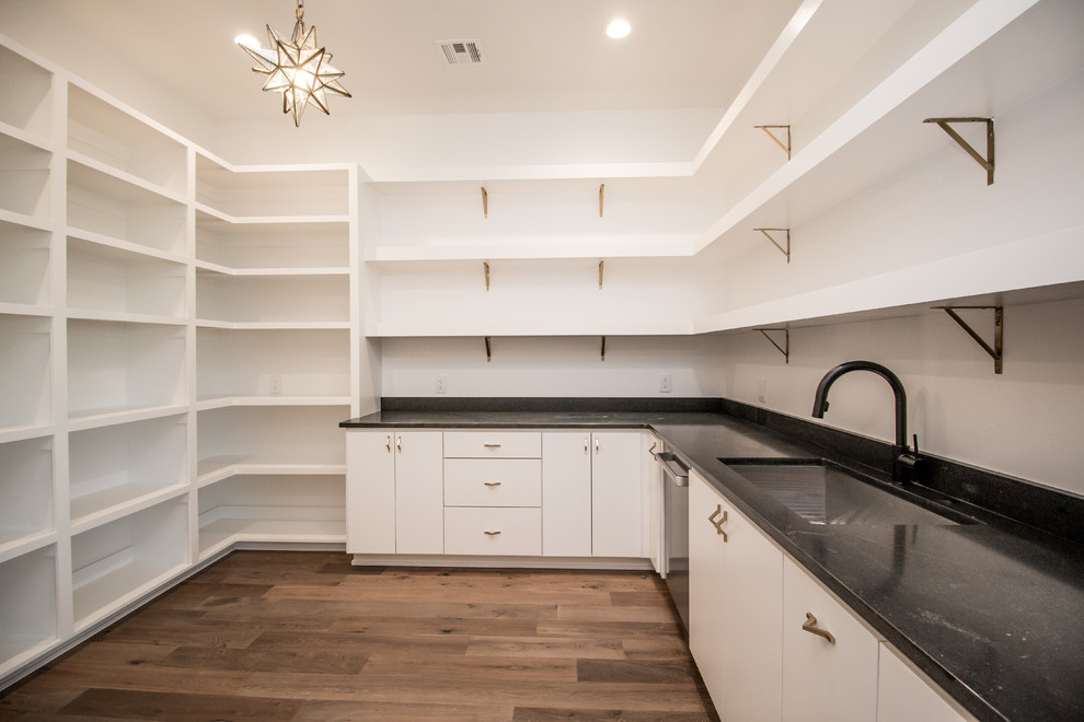 This is an example of an expansive contemporary u-shaped kitchen pantry in Other with an undermount sink, flat-panel cabinets, white cabinets, quartzite benchtops, stainless steel appliances, medium hardwood floors, with island, brown floor and black benchtop.