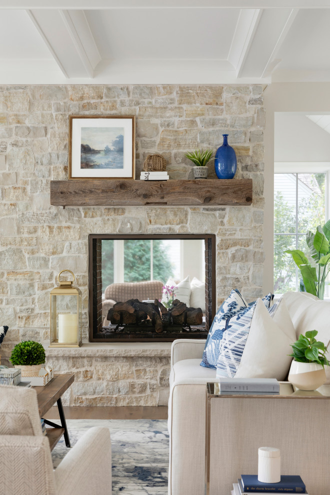 Example of a large classic open concept medium tone wood floor and gray floor living room design in Minneapolis with beige walls, a two-sided fireplace, a stone fireplace and a concealed tv