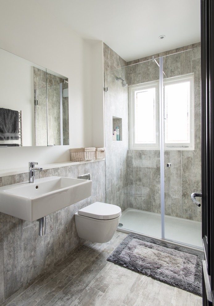 Inspiration for a mid-sized contemporary 3/4 bathroom in London with a wall-mount toilet, a wall-mount sink, grey floor, an alcove shower, gray tile and white walls.