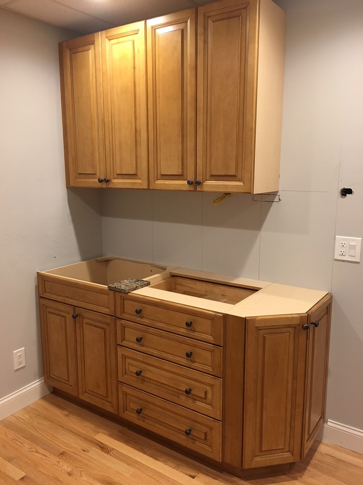 Small traditional galley kitchen pantry in New York with an undermount sink, raised-panel cabinets, medium wood cabinets, quartz benchtops, beige splashback, ceramic splashback, stainless steel appliances, light hardwood floors, no island, brown floor and brown benchtop.