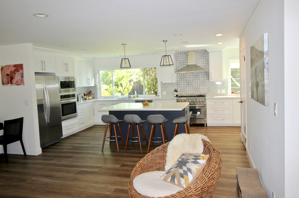 This is an example of a large transitional l-shaped open plan kitchen in San Francisco with an undermount sink, shaker cabinets, white cabinets, quartz benchtops, blue splashback, ceramic splashback, stainless steel appliances, vinyl floors, with island, brown floor and grey benchtop.
