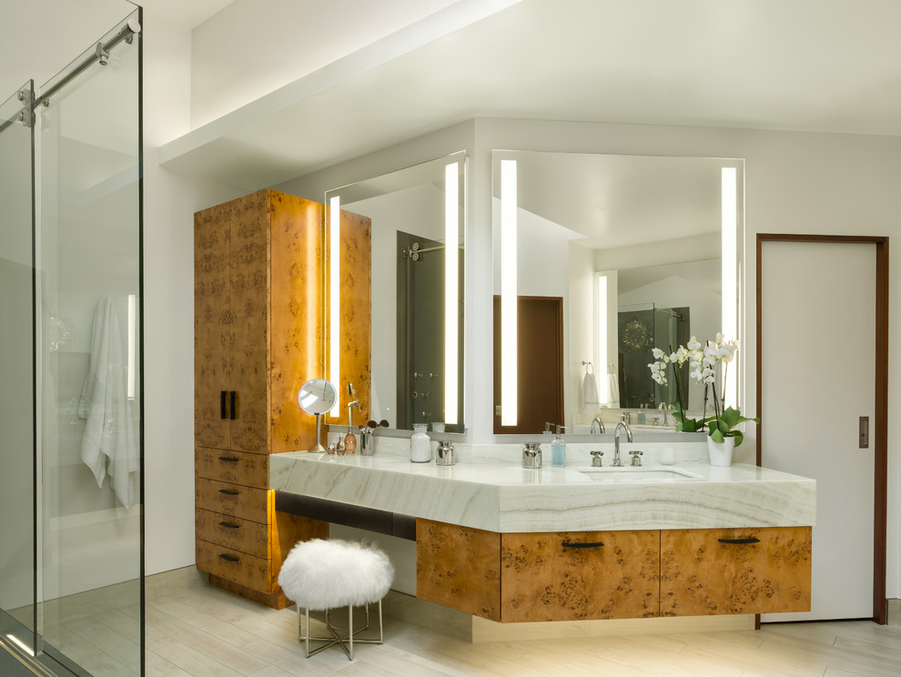 This is an example of a mid-sized contemporary master bathroom in Other with flat-panel cabinets, light wood cabinets, a freestanding tub, a corner shower, gray tile, porcelain tile, white walls, porcelain floors, an undermount sink, onyx benchtops, beige floor, a sliding shower screen and white benchtops.