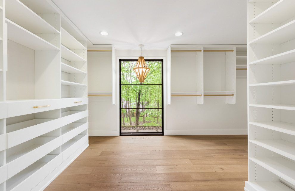 Photo of a large midcentury gender-neutral walk-in wardrobe in Minneapolis with open cabinets, white cabinets, medium hardwood floors and brown floor.
