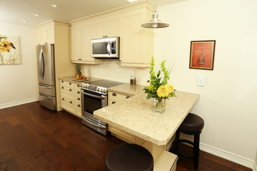 Inspiration for a small transitional galley medium tone wood floor and brown floor enclosed kitchen remodel in Toronto with a double-bowl sink, shaker cabinets, beige cabinets, quartz countertops, beige backsplash, ceramic backsplash, stainless steel appliances and a peninsula