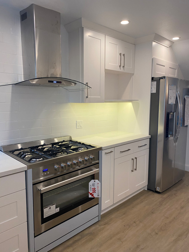 This is an example of a mid-sized scandinavian galley separate kitchen in Los Angeles with shaker cabinets, white cabinets, quartzite benchtops, white splashback, subway tile splashback, stainless steel appliances, vinyl floors, no island, brown floor and white benchtop.