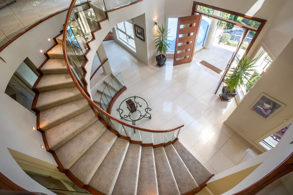 Large contemporary carpeted curved staircase in Sydney with carpet risers and glass railing.