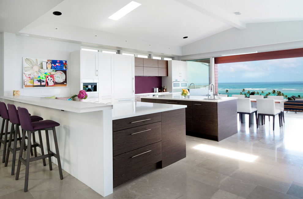 This is an example of a large modern l-shaped eat-in kitchen in Hawaii with flat-panel cabinets, beige cabinets, stainless steel benchtops, glass sheet splashback, white appliances, concrete floors and grey floor.