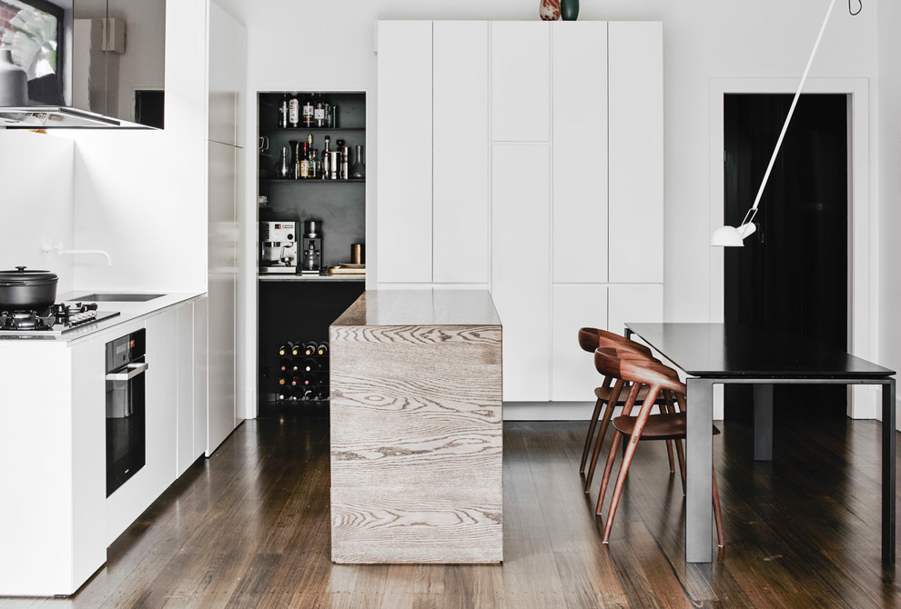 This is an example of a contemporary l-shaped eat-in kitchen in Melbourne with flat-panel cabinets, white cabinets, white splashback, dark hardwood floors, with island, brown floor and white benchtop.