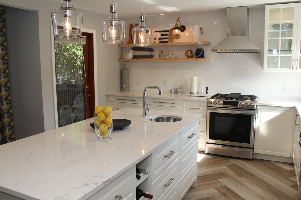 Open concept kitchen - large transitional l-shaped vinyl floor and brown floor open concept kitchen idea with an undermount sink, recessed-panel cabinets, white cabinets, quartz countertops, white backsplash, ceramic backsplash, stainless steel appliances and an island