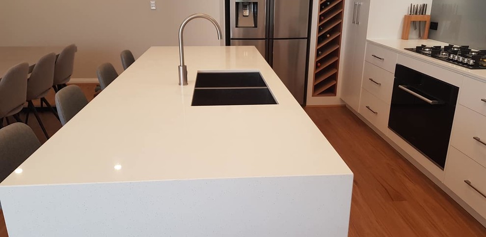Inspiration for a mid-sized modern galley eat-in kitchen in Other with an undermount sink, flat-panel cabinets, white cabinets, quartz benchtops, grey splashback, glass sheet splashback, stainless steel appliances, laminate floors, with island and white benchtop.