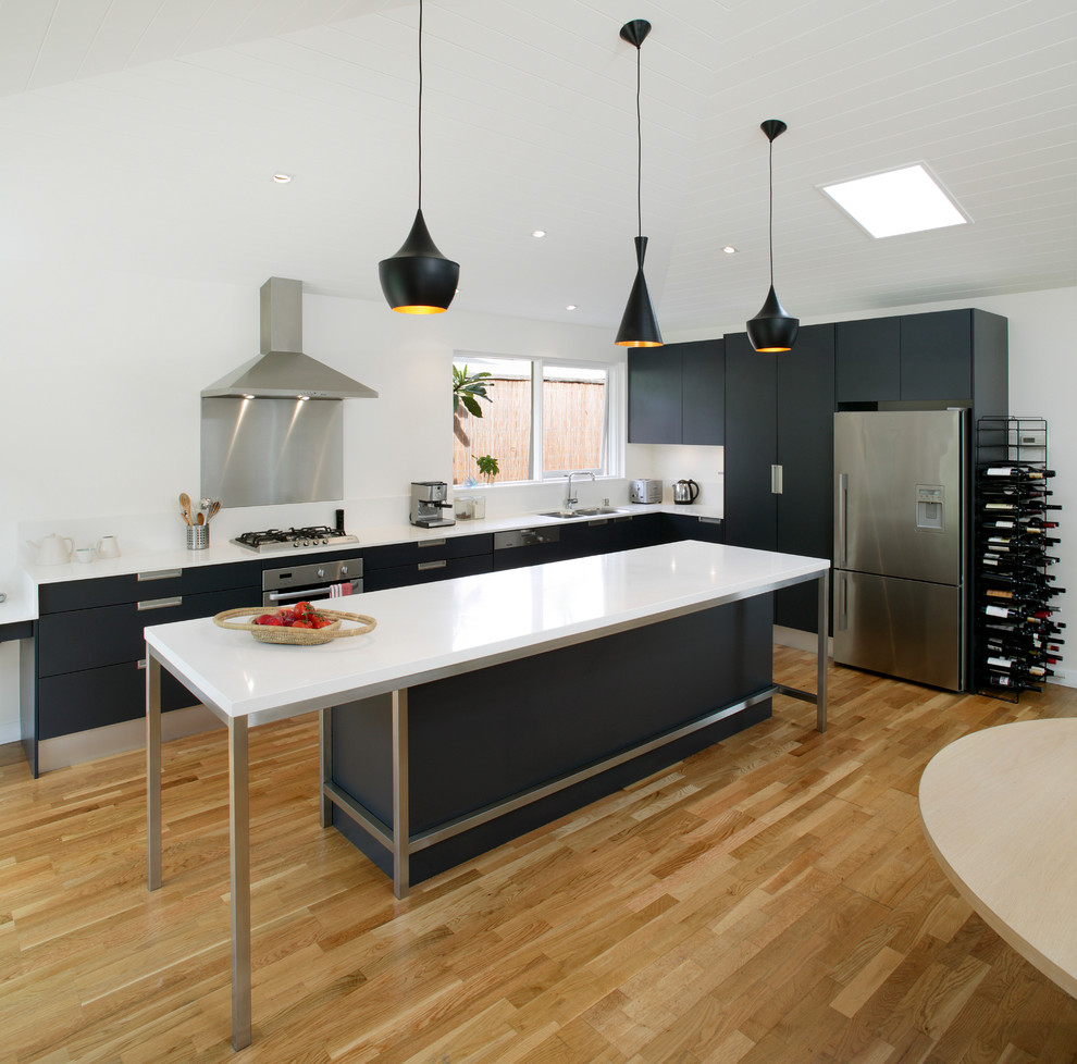 This is an example of a mid-sized contemporary l-shaped open plan kitchen in Sydney with a double-bowl sink, recessed-panel cabinets, black cabinets, quartz benchtops, white splashback, ceramic splashback, stainless steel appliances, light hardwood floors and with island.